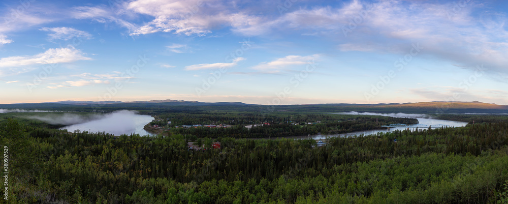 Panoramic Aerial View of a small town, Pelly Crossing, during a sunny and cloudy sunrise. Located in Yukon, Canada.