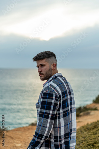 Hombre joven adolescente modelo con camisa azul de cuadros posando en la costa y playa 