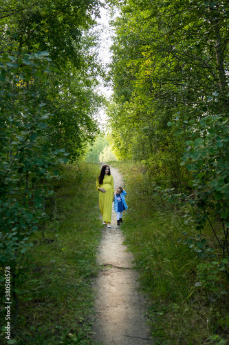 Pregnant woman in yellow dress with her daughter in nature