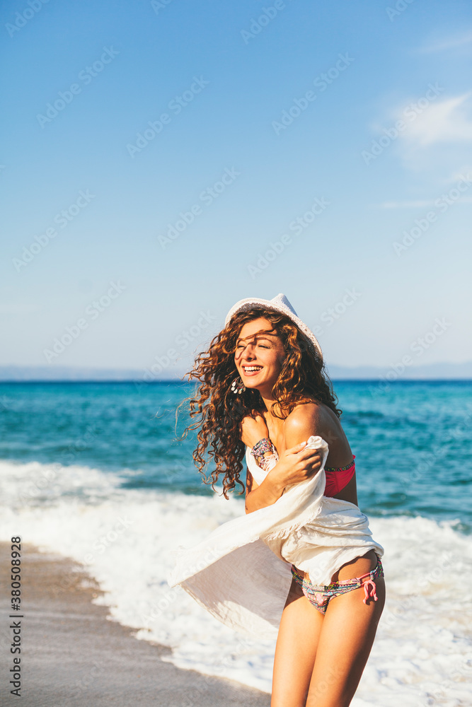 Attractive woman with white scarf and hat, enjoying the water and the sunlight on the beach