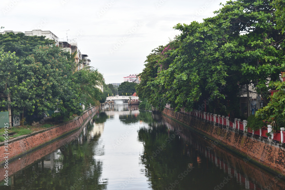 Canal with brown brick walls and green plants reflecting on the water surface, View from the bridge in Bangkok, Thailand