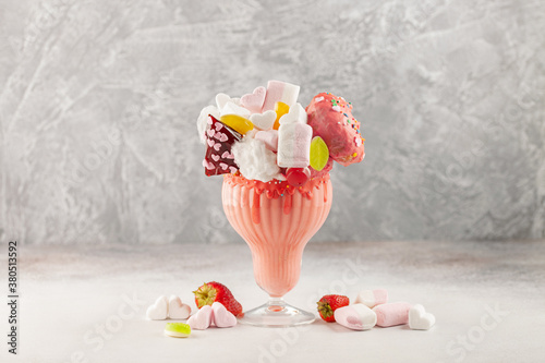 Extreme milkshake. Freakshake. Pink strawberry monstershake with sweets on grey background.  Overshake photo