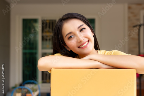 Customer woman get satisfied and happy of courier service when she get parcel box very quickly from delivery service. Pretty girl stand in fron of house with cardboard box and smile face.