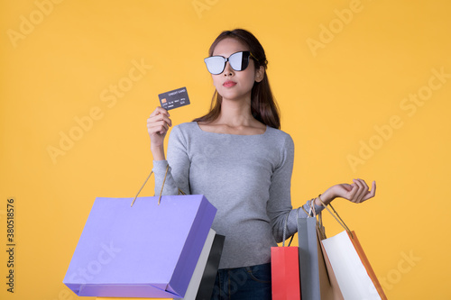 Beautiful young Asian woman with colourful shopping bags and credit card isolated on yellow background