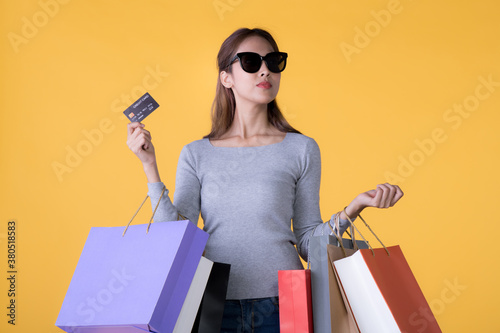 Beautiful young Asian woman with colourful shopping bags and credit card isolated on yellow backgroun