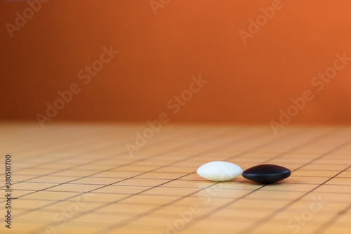 Black and white stones on the playing field (gohan) of Chinese game go, orange background