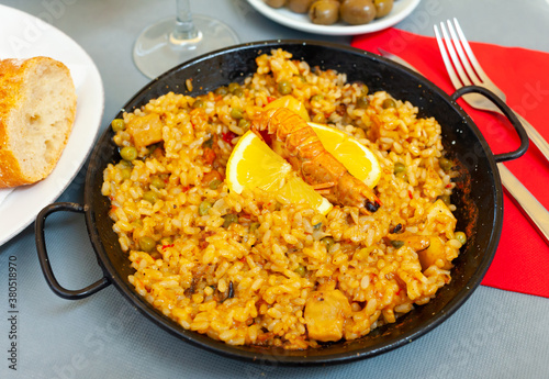 Delicious seafood paella - savory rice dish with shrimps and clams served with lemon slice in traditional paella pan