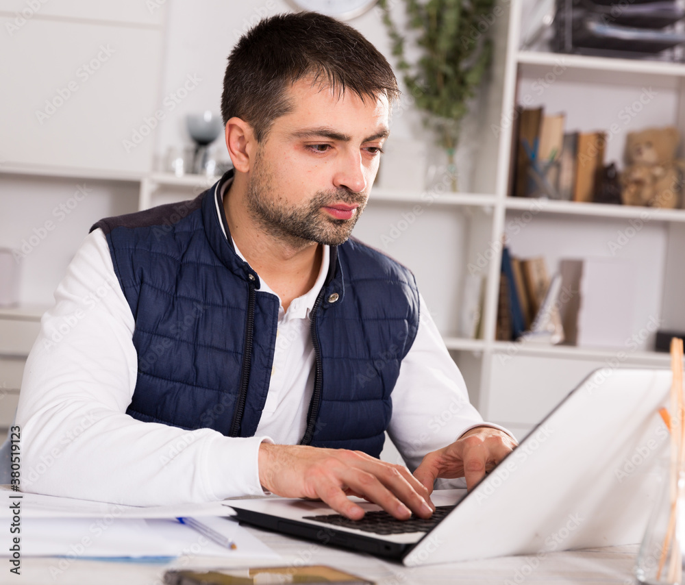 Young businessman in shirt working with laptopt and documents at the table