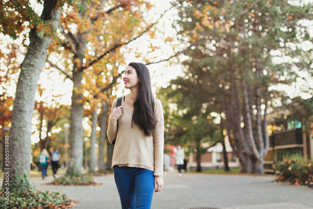 Young mixed race woman - asian & caucasian - walking outside with backpack on fall day Young mixed race woman - asian & caucasian - walking outside with backpack on fall day