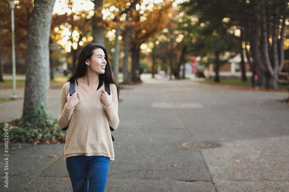 Young mixed race woman - asian & caucasian - walking outside with backpack on fall day Young mixed race woman - asian & caucasian - walking outside with backpack on fall day