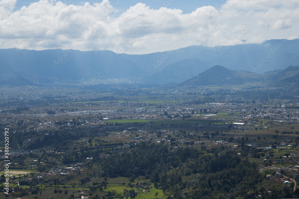 Beautiful landscape of a small town seen from the top of the mountain - rural town surrounded by trees, mountains and a volcano on a sunny day with clouds - landscape in Quetzaltenango 