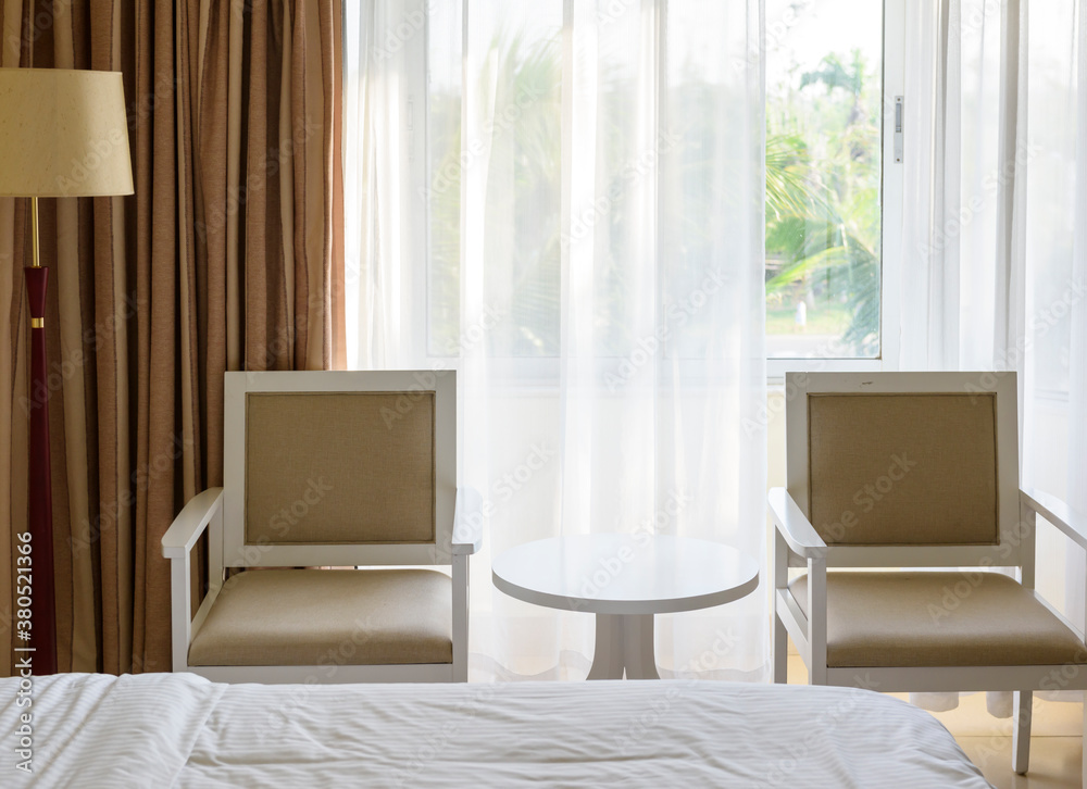 Interior decor concept . Two wooden armchairs flanking a small round side table in front of large windows. Interior decor concept . Two wooden armchairs flanking a small round side table in front of large windows.