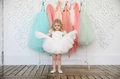 fancy dresses for girls. baby in a white, lush, elegant dress near the hanger with festive clothes. fashion for children. shop. photo