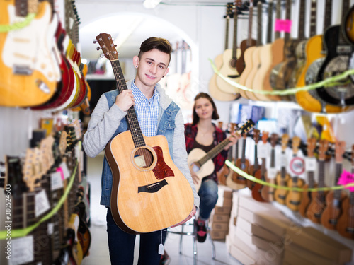 Glad teenage boy and girl choosing best acoustic guitar in guitar shop
