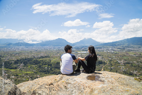 Young couple sitting on the top of the mountain enjoying nature  young people on the edge of the cliff observing the valley enjoying a day outdoors,  landscape in Quetzaltenango Guatemala. © Fernanda