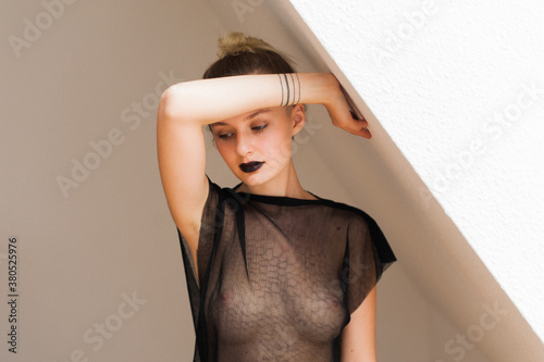 Fashionable Millennial Woman in a Sheer Black Dress in a Room with White Walls