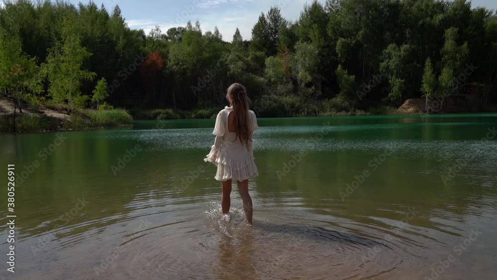 one young woman in a white dress goes and wets her feet on a wild forest lake in summer. one young woman in a white dress goes and wets her feet on a wild forest lake in summer.