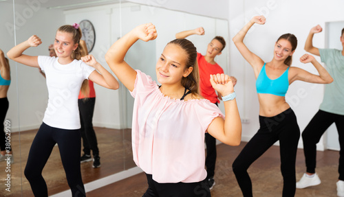 Smiling teen girl enjoying while training movements of modern group dance in choreography class