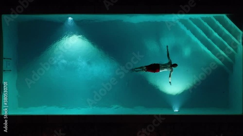 Aerial top shot view of young male adult jumping diving swimming pool at night in tuscany italy shot in 4k
