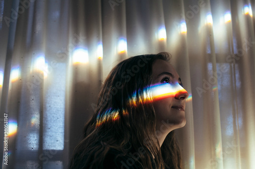 Teenage girl looking forward with a rainbow glowing prism on her face