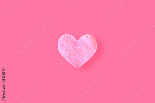A heart shaped stone on a pink background.