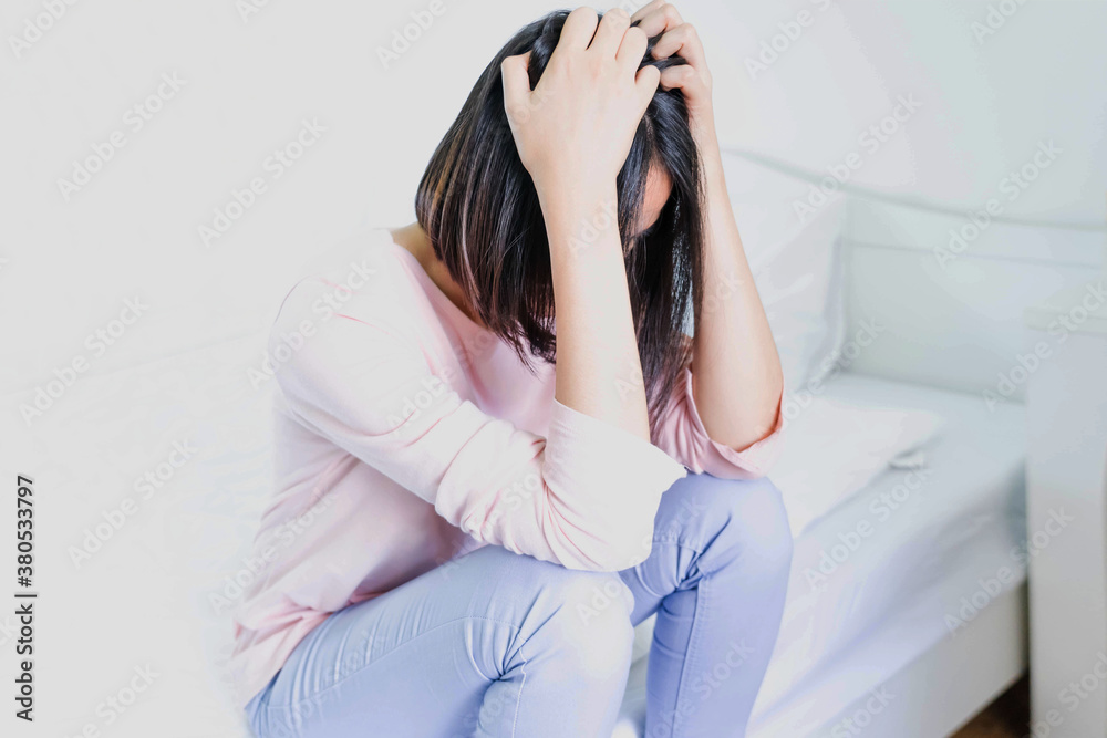Upset depressed young woman sitting on bed feeling strong headache migraine, sadness Upset depressed young woman sitting on bed feeling strong headache migraine, sadness