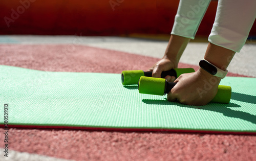 Small green dumbbells in hands on a green mat
