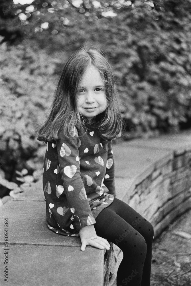 Black and white portrait of a beautiful young girl sitting on a stone wall Black and white portrait of a beautiful young girl sitting on a stone wall