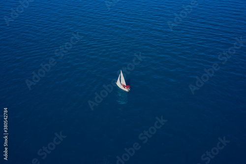 White sailboat on blue water. Sailboat with red trim. Top view of a boat with sails.