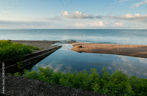 The river flows into the sea. Quiet river water and endless sea across a small isthmus of a pebble beach. Blue sky with clouds. The river Psyrtskha, New Athos, Abkhazia. photo