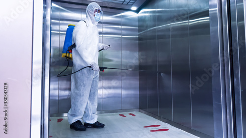 Worker in personal protective equipment (ppe) suit cleaning in building with spray disinfectant water to remove covid 19