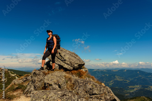 Young man with a backpack standing on top of a mountain and enjoying the view of the valley, the top of the Carpathians Eared stone.