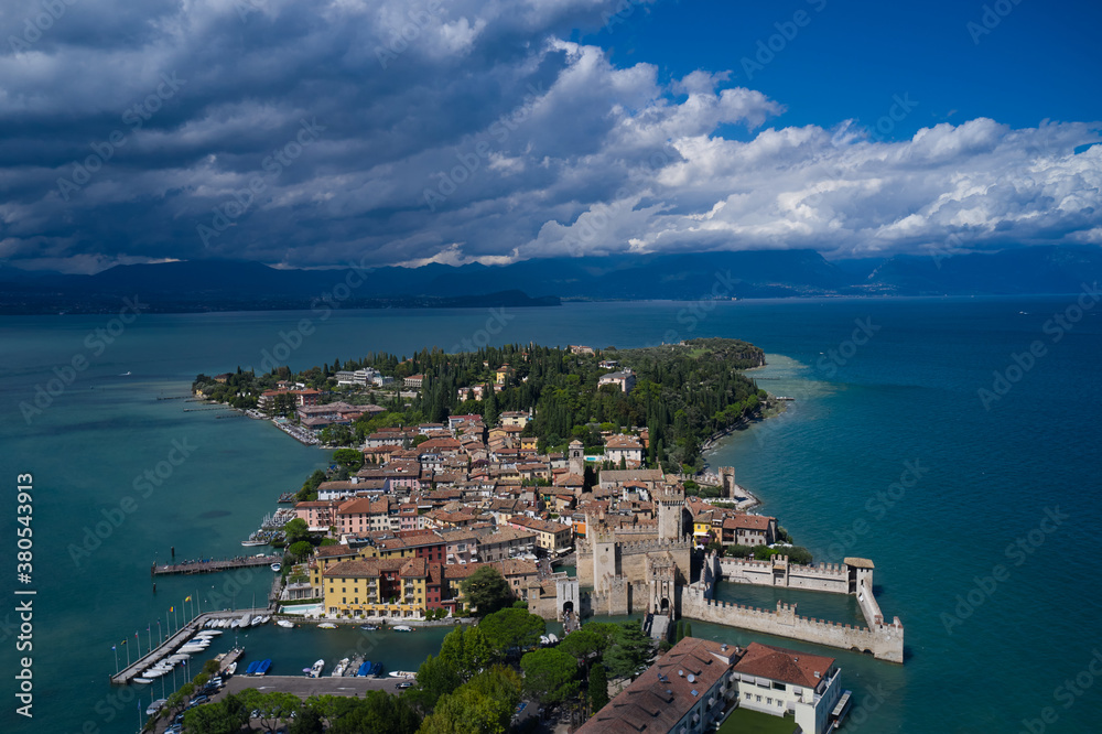 Aerial view on Sirmione sul Garda. Italy, Lombardy.  Cumulus clouds over the island of Sirmione. Aerial photography with drone.  Panoramic view at high altitude.  Rocca Scaligera Castle in Sirmione.