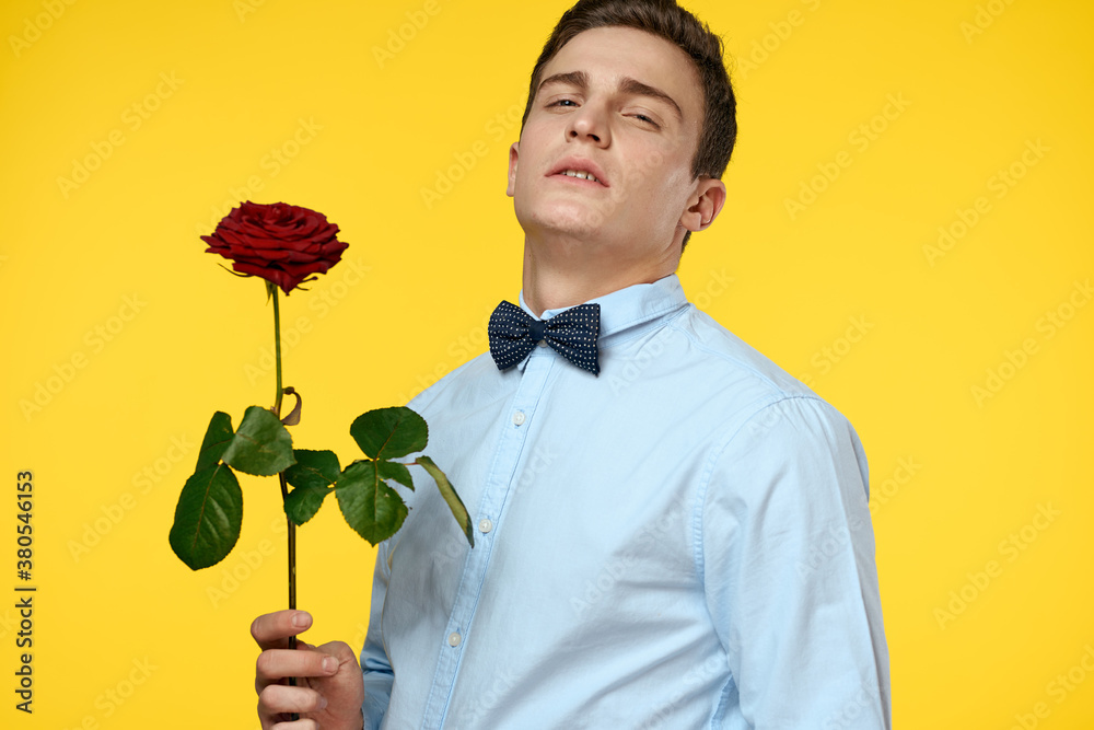 Gentleman in shirt and bow tie around his neck yellow background red rose