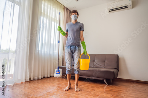 Young man with mop cleaning floor at home during coronavirus COVID 19