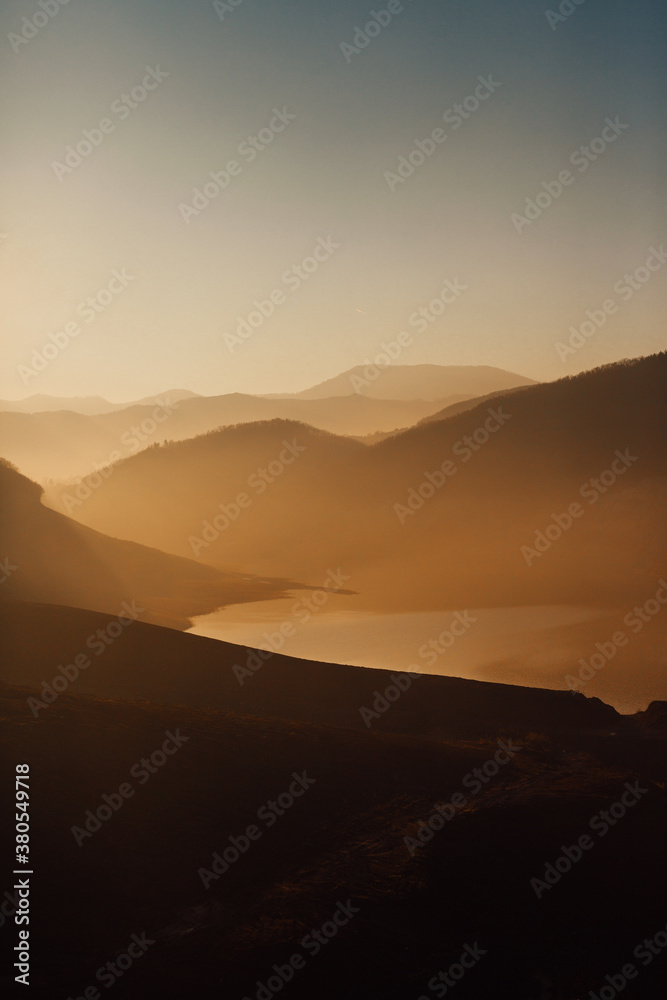 Beautiful sunset above the lake and mountains covered with light fog Beautiful sunset above the lake and mountains covered with light fog