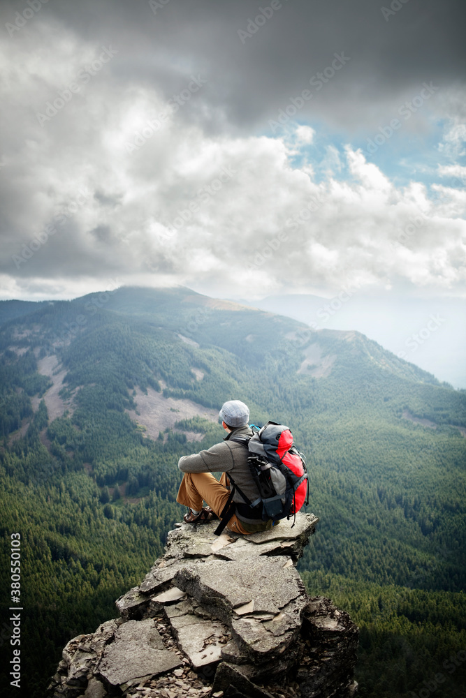 Man sitting on cliff up high overlooking forests Man sitting on cliff up high overlooking forests
