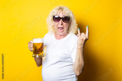 Φωτογραφία Surprised blonde old woman holding a glass of beer and showing a rocker goat on