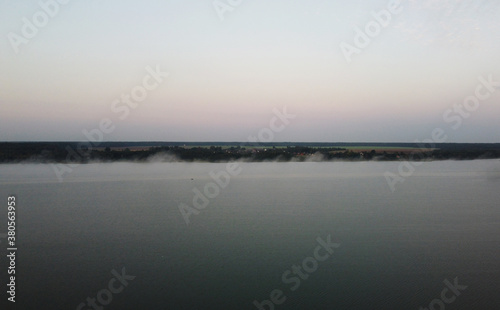 Top view of fog at sunrise over calm lake and forest