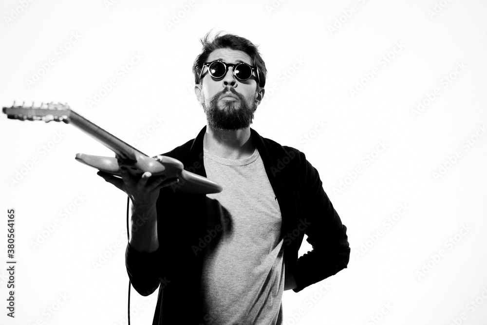 A man holds a guitar in his hands black leather jacket dark glasses music performance light background A man holds a guitar in his hands black leather jacket dark glasses music performance light background