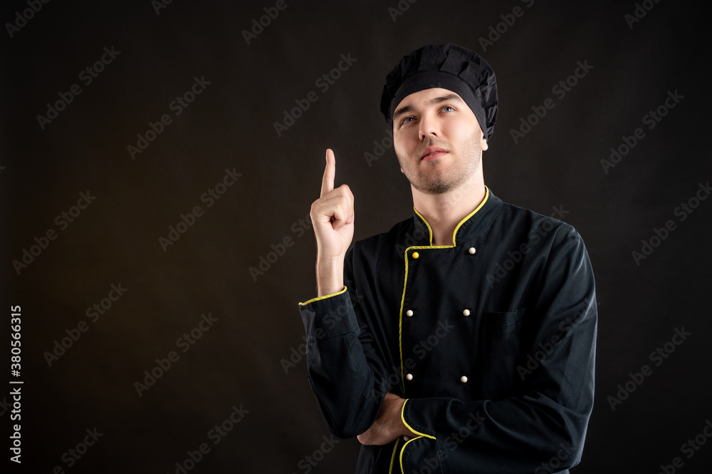 Young male dressed in a black chef suit with his finger up has come up with an idea Young male dressed in a black chef suit with his finger up has come up with an idea