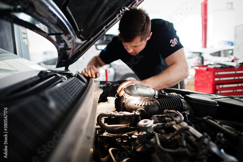 Car repair and maintenance theme. Mechanic in uniform working in auto service, checking engine. © AS Photo Family