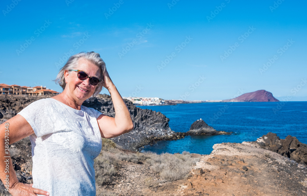 Attractive senior woman white haired standing on the cliffs enjoying vacation or excursion and freedom in seascape. Active retired elderly people