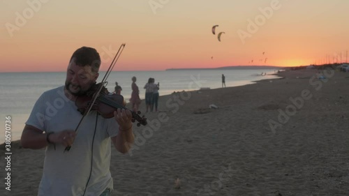 Man enjoys playing violin on the beach during beautiful sunset. Gorgeous summer evening