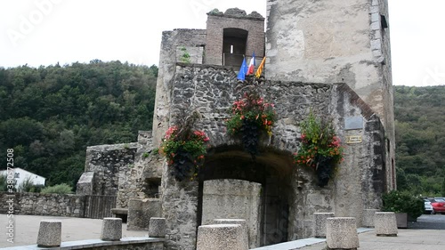 Still image of the entrance to the fortress within the medieval village of Prats de Mollo la Preste, in it you can see several red flowers and the Catalan, French and European flags photo