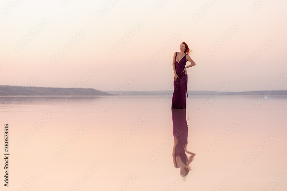 A beautiful young woman posing at sunset in the water with a reflection