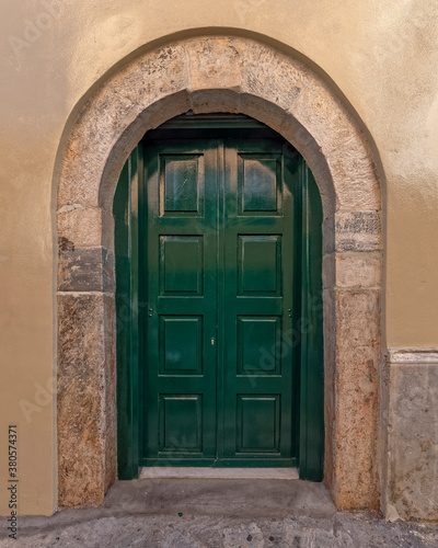 dark green painted door with arched stone frame © Dimitrios