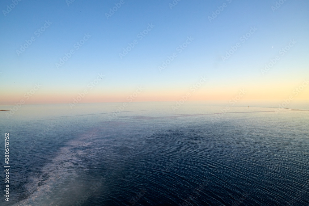View on water of sea and pink and yellow sunset on horizon in background View on water of sea and pink and yellow sunset on horizon in background