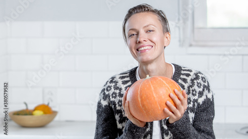 Beautiful woman in sweater with orange pumpkins in white kitchen