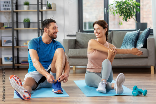 sport, fitness, lifestyle and people concept - smiling man tying laces and woman stretching at home photo